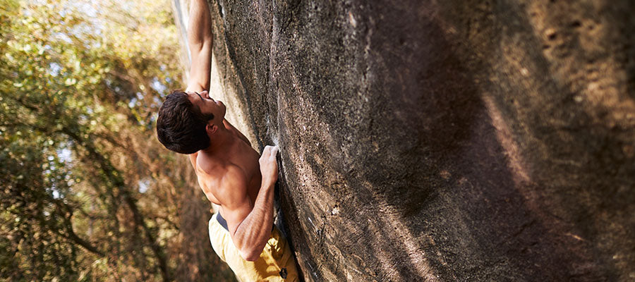 Athletic Male climbing the side of a cliff over a forest.