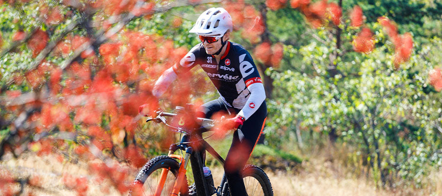 Male Cyclist ridding in a field near red flowers.