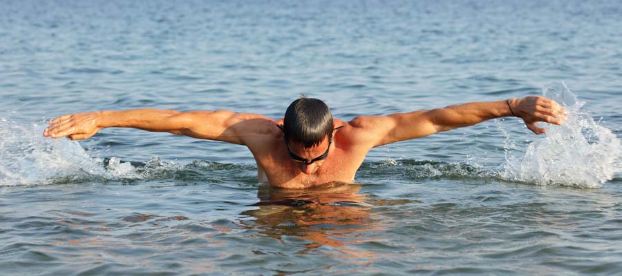 Athletic male doing the breast stroke in a large body of water.