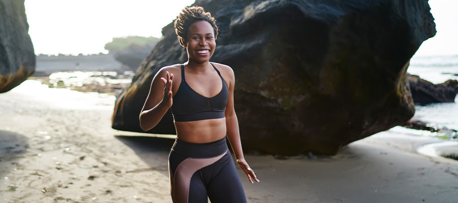 Athletic woman on the beach with large rocks behind her.