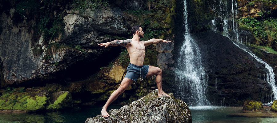 Athletic Male performing Tai Chi on a rock next to a small waterfall.