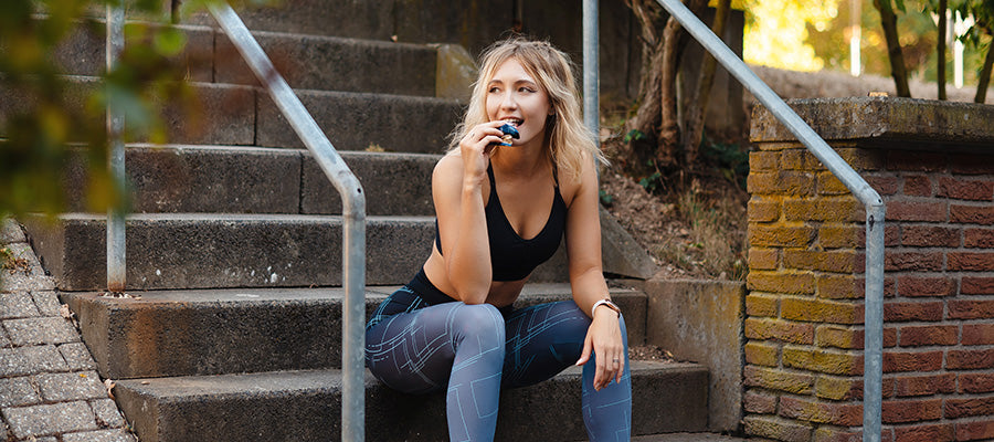 athletic woman resting on stairs after a workout enjoying a BodyHealth Bar