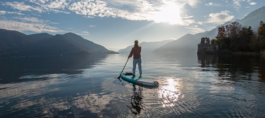 Person paddle boarding on a calm river with light fog in the distance.