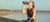Athletic woman drinking from a shaker bottle next to a large lake.