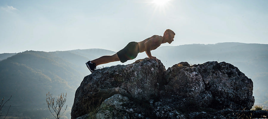 Athletic man doing planks on a rock a top a mountain.