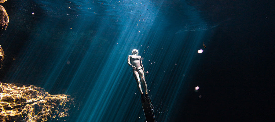 Free diver under water, heading to the surface surrounded by darker waters.
