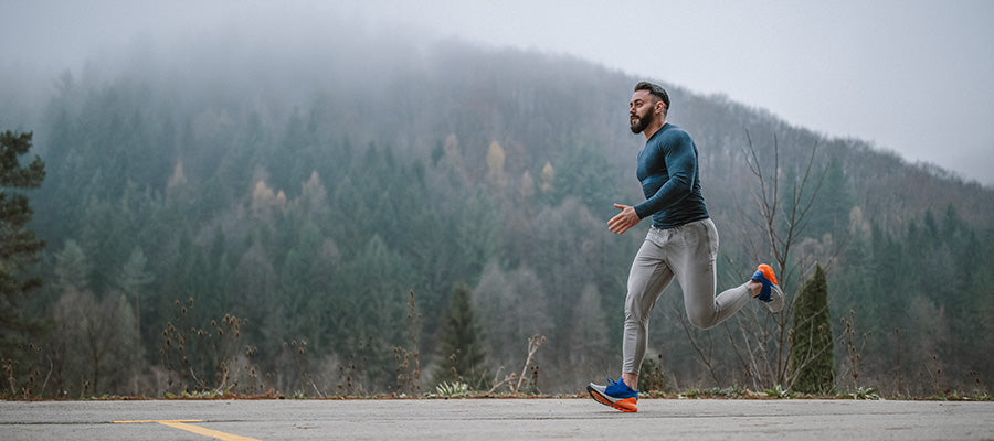 Athletic male running through the hills with a foggy hill top behind him.