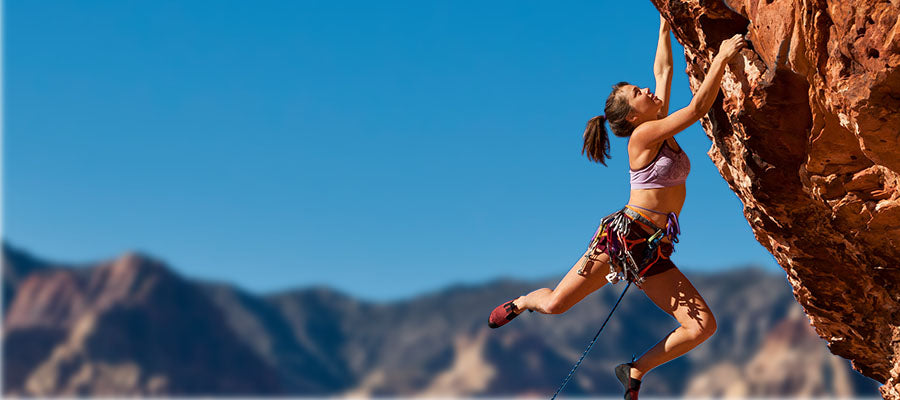 Woman free climbing on a cliff with mountains in the background.