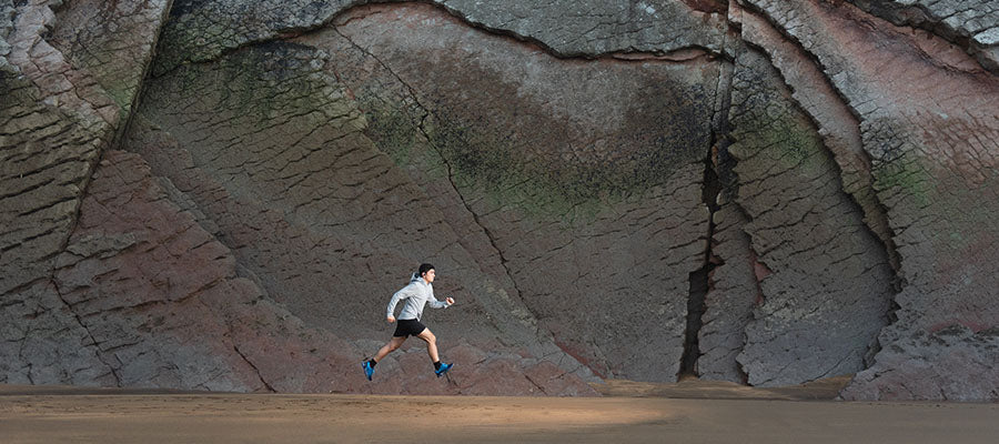 Athletic person running in front of a large rock wall.