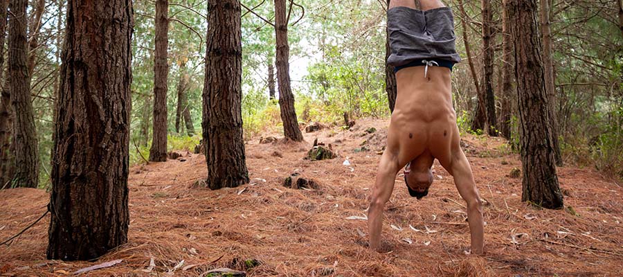 Athletic male doing handstands in the middle of a forest.