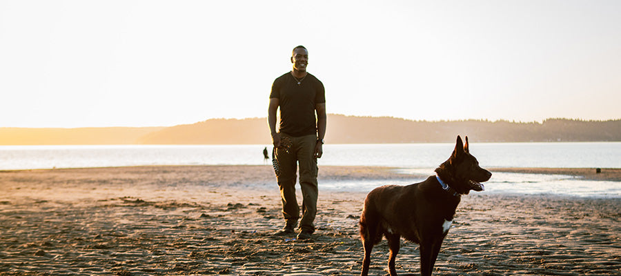Athletic man walking his German Shepperd on the beach during sunrise.