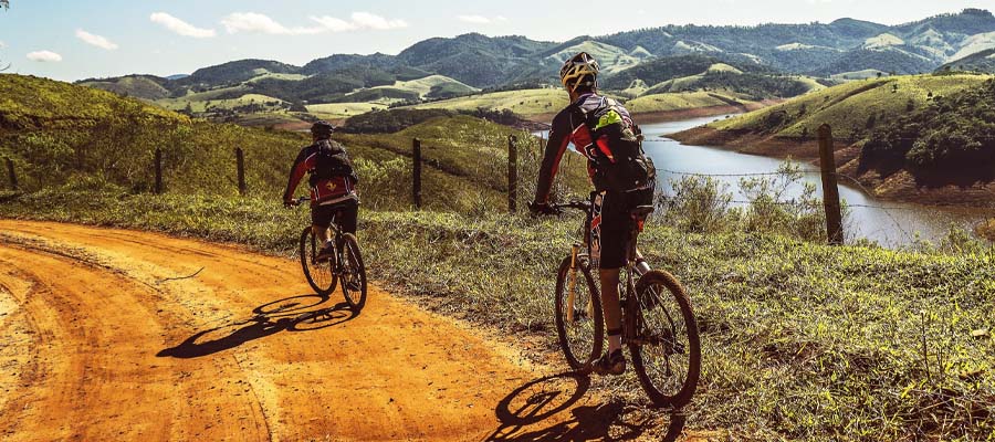 Two mountain bikers traversing a dirt path near a river.