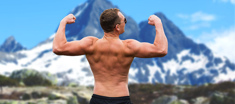 Male bodybuilder showing off his shoulder muscles with a blue snowy mountain in the background.