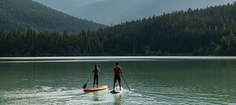 Two people on a lake in the mountains paddle boarding.