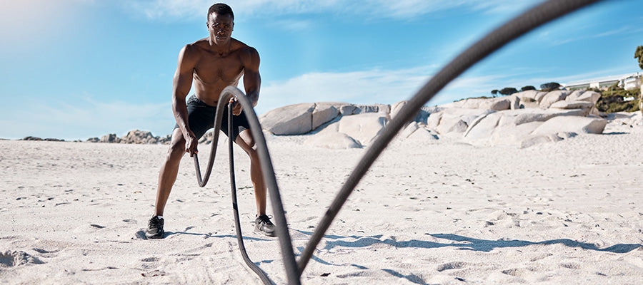Athletic male using battle ropes for exercise on the beach.