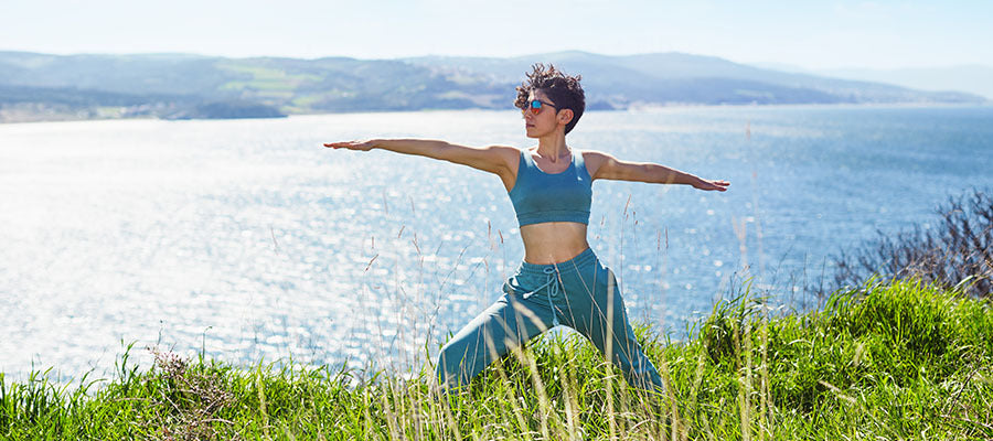 Woman doing yoga lakeside on a sunny day in a green field.