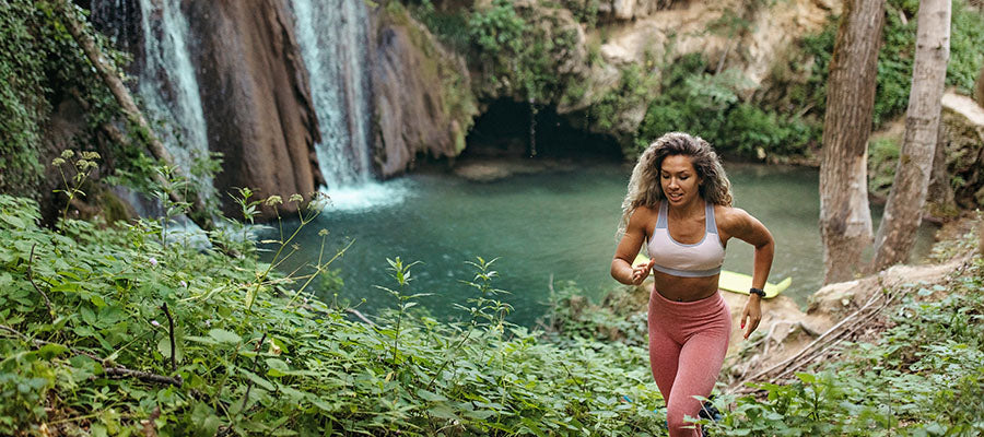 Athletic woman traversing up a mountain side with a waterfall in the background.