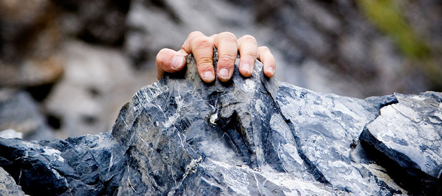 Person's hand holding on the a dark rock as if pulling themselves up.