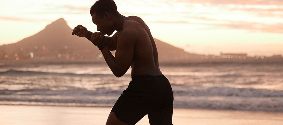 Athletic person practicing shadow boxing on the beach during sunrise.