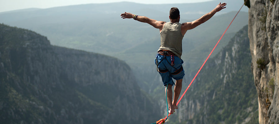Athletic man walking a tight rope over a large canyon.