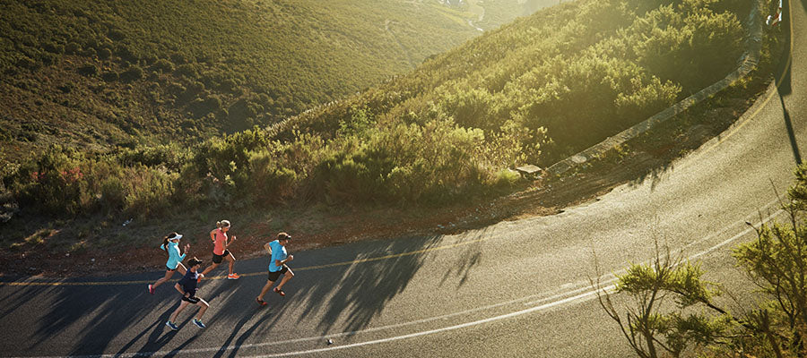 Aerial shot of a group of runners running on a road in the mountain.