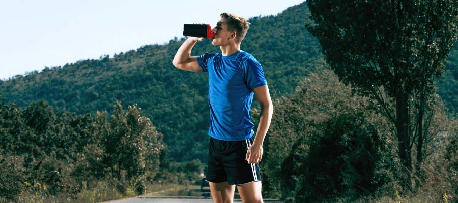 Athletic male taking a break to drink from his shaker bottle while he is in nature.