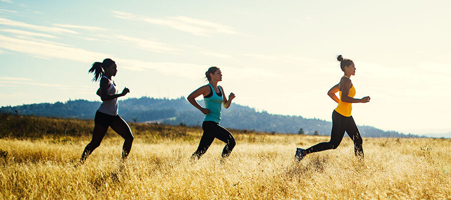 Athletic women running through yellow fields with a mountain in the background.