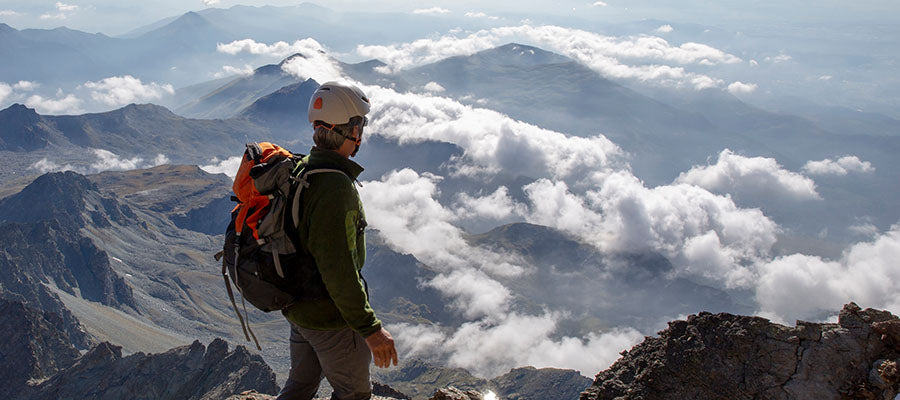 Mountain climber standing on a peak overlooking a cloudy mountain side.