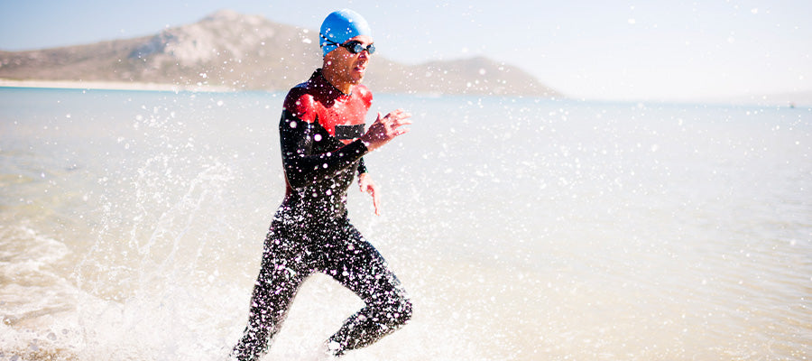 Athletic person running on the beach in the water while wearing a wetsuit.