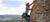 Athletic female rock climber scaling a mountain with a smaller mountain range in the distance.