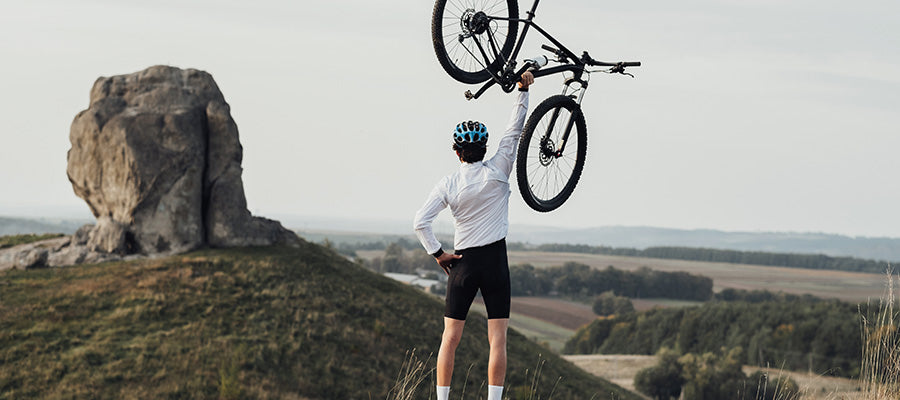 Cyclist triumphantly holding their bike in the air after reaching the mountain summit.