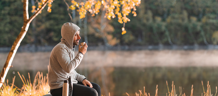 Athletic male drinking a warm drink on a chilly fall day next to a foggy river.