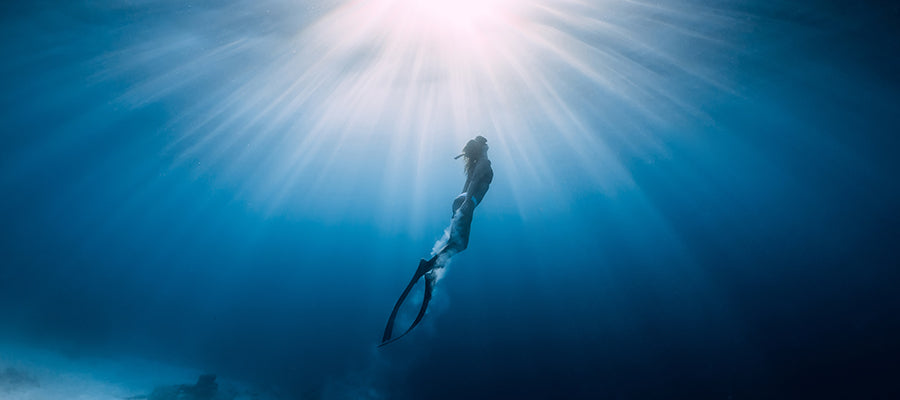 Person free diving in beautiful blue waters and sun rays.