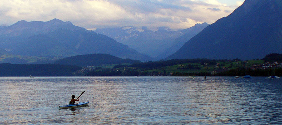 Person kayaking on a lake surrounded by mountains.