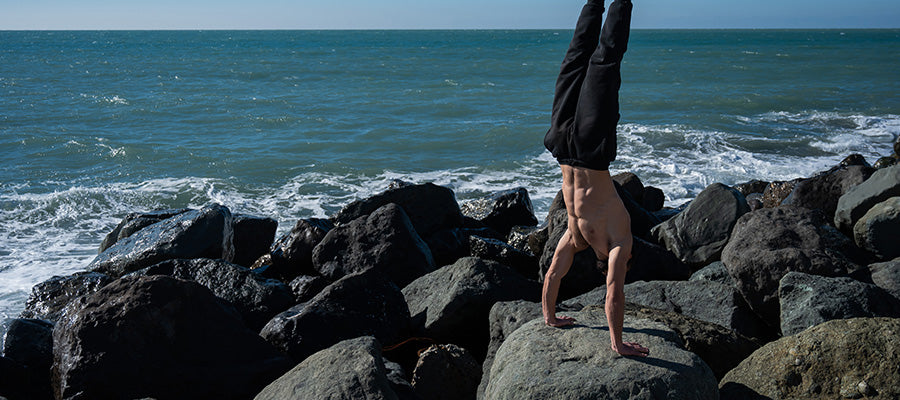 Athletic man doing yoga on rocks next to the shoreline.