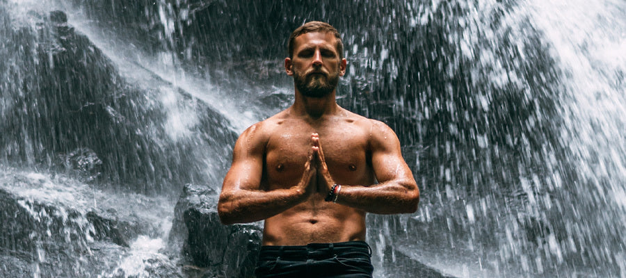 Athletic man doing meditation under a flowing waterfall.