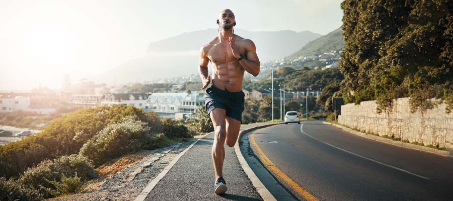 Athletic male running on the road next to a mountain with a small city in the background.