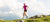 Person jogging in nature with blue mountains and clouds behind them.
