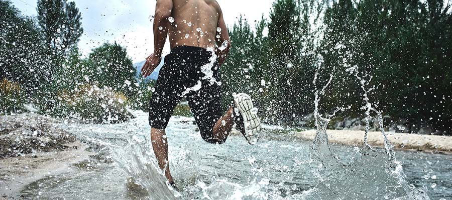 Athletic Person running on the bank of a river with water spray behind them.