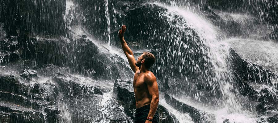 Athletic male stretching next to a waterfall on a mountain side.