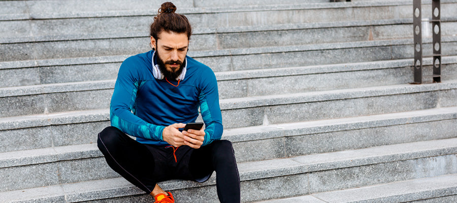 An athletic man resting on steps checking his smart phone.