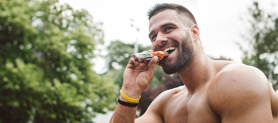 Athletic male eating a protein bar while in nature.