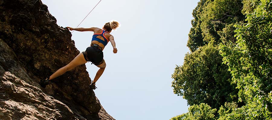 Athletic woman free climbing and cresting the top of the mountain she is on.