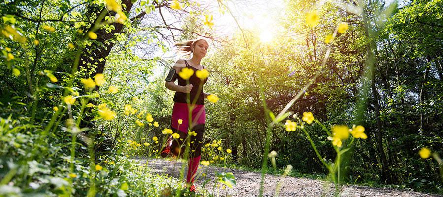 Athletic woman jogging in the sunshine on a dirt path surrounded by yellow flowers.
