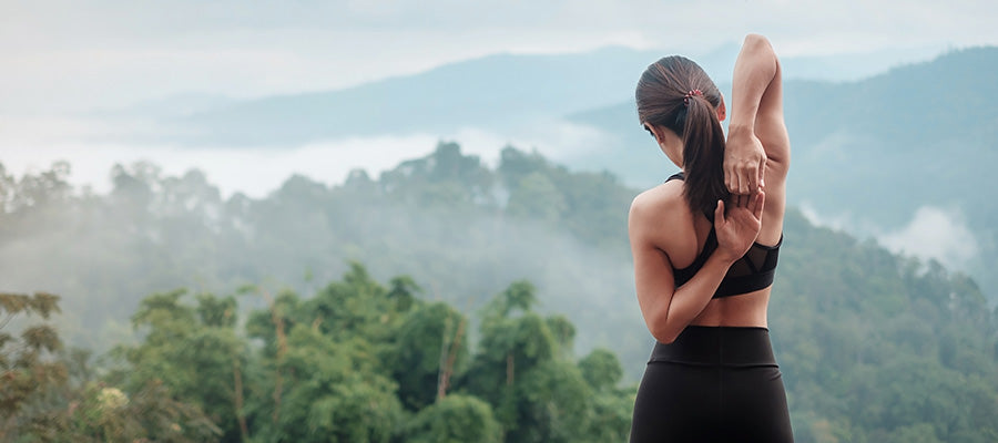 Athletic woman stretching on top of a hill looking out to a foggy mountain side.