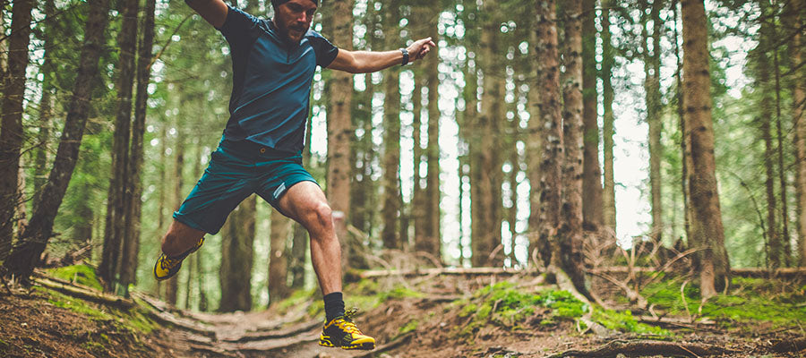 Athletic man jumping on a forest path from a higher vantage.