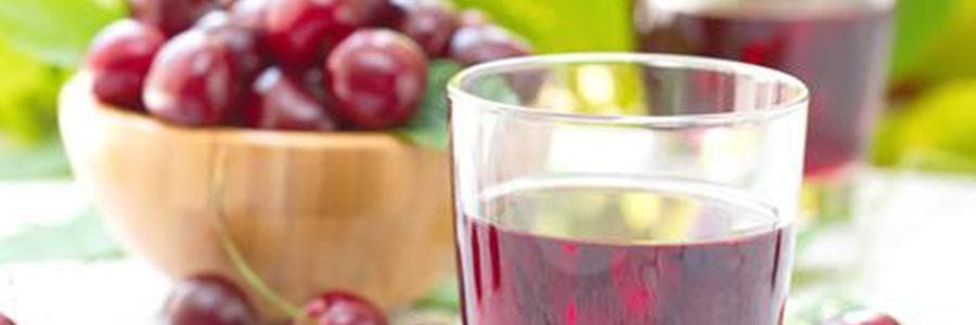 A wooden bowl of tart cherries and a glass of cherry juice.