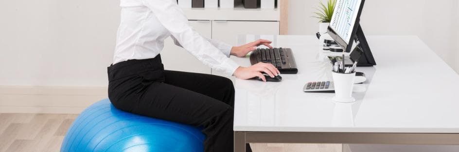 Person sitting on a yoga ball while working in the office.