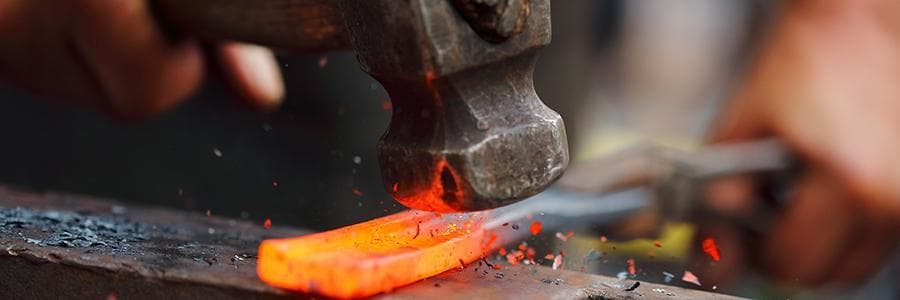 A person blacksmithing a metal tool. Close up of hot metal and hammer.